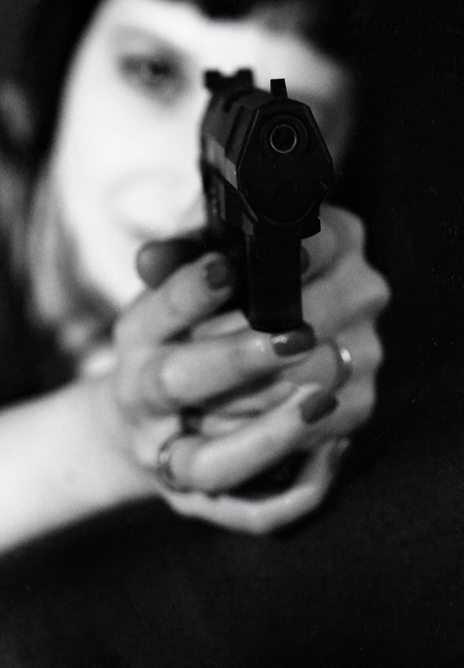 Woman aiming a handgun toward the camera in shallow focus, black and white portrait photography, London, 2004
