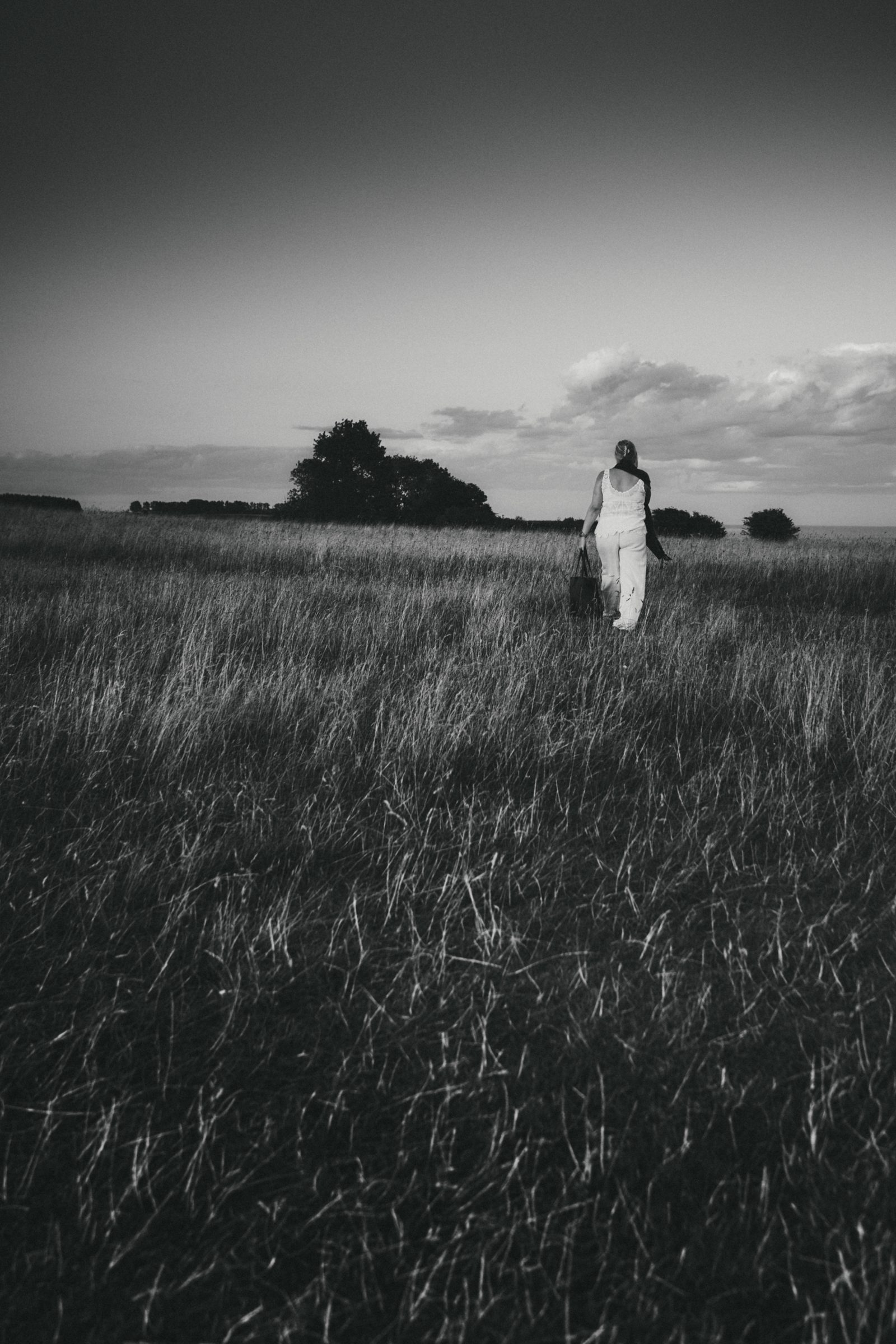 Figure in white walking through tall grass toward the horizon, black and white portrait photography, Ale’s Stenar, Kåseberga, Sweden, 2026